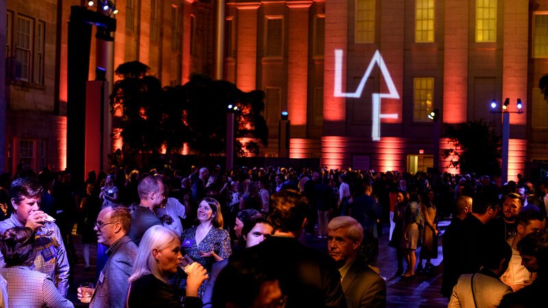 With a projection of the LAF logo on the wall in the background, attendees at LAF's 2024 Annual Benefit cluster in small groups.