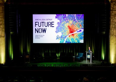 Barbara Deutsch stands at a podium on a stage with a large screen that says "Future Now" in the background