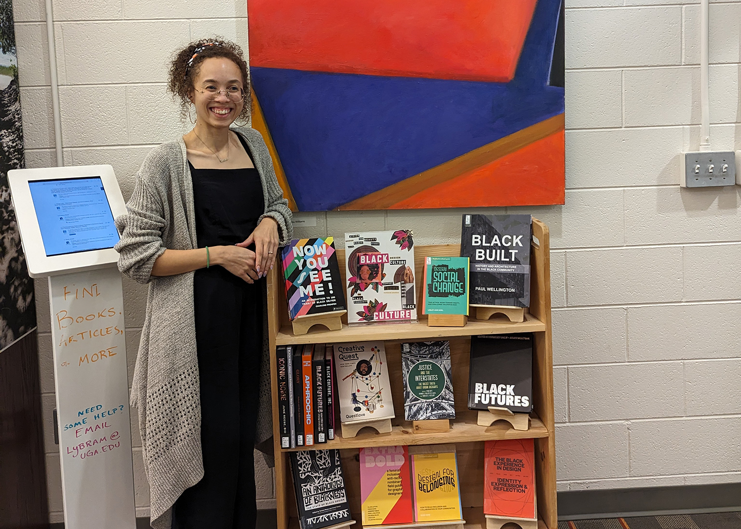 Sam Nash Riggs standing in front of a bookshelf with books by black authors about design.