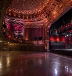 Ornate historic theater interior with gilded details, red lighting, and a stage set for an event